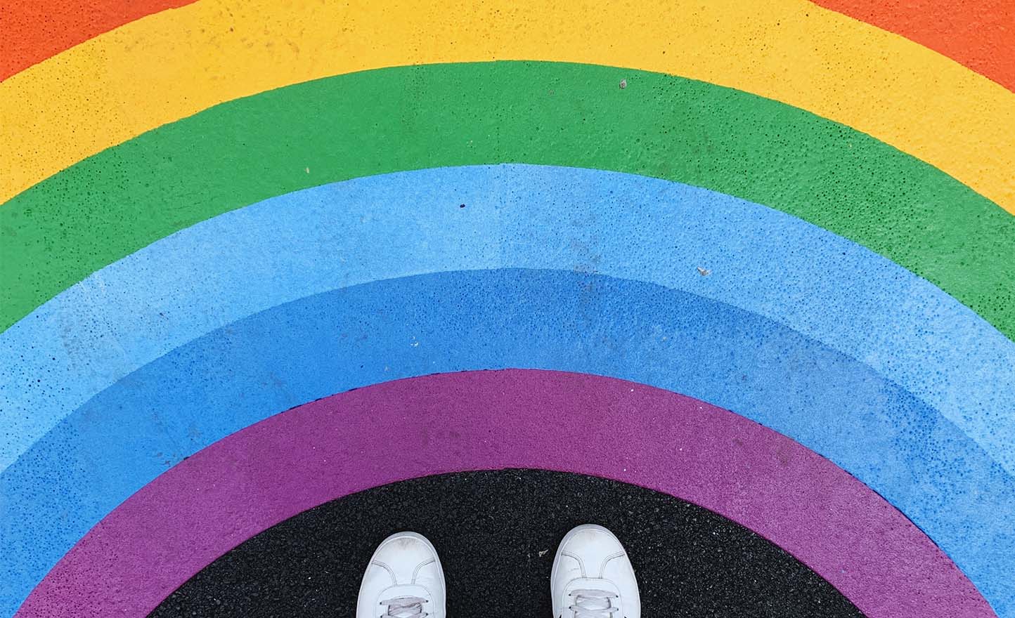 A rainbow painted on pavement, and feet standing on it