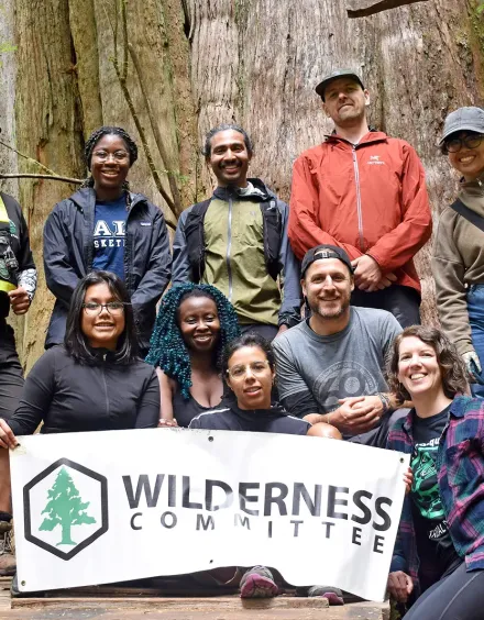 Wilderness Committee Group standing in front of a large tree with a sign featuring the company logo